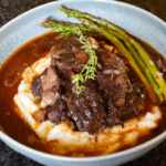 Short ribs in a low bowl with mashed potatoes and asparagus